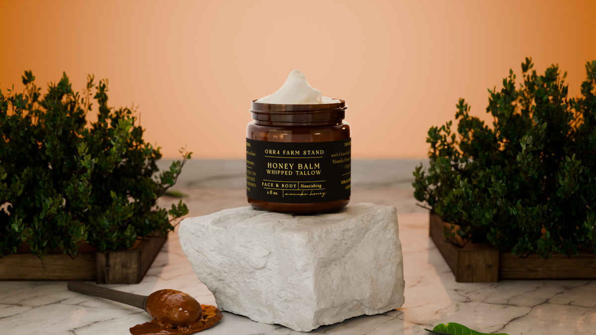 Open Manuka Honey Balm jar on a white stone block between potted plants.