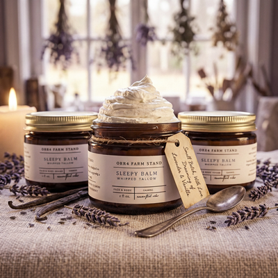 Sleepy Balm jars with lavender, vanilla pods and a spoon on linen beside a window.